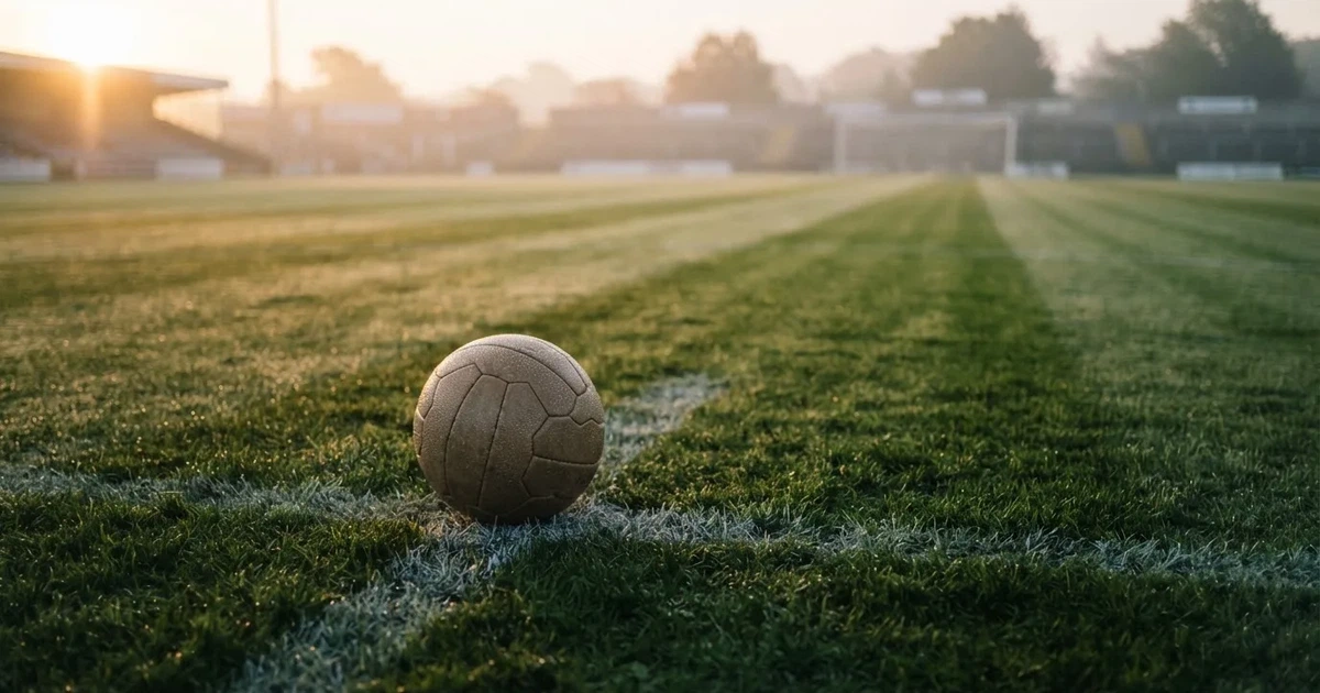 Een voetbal op de middenstip van een grasveld in het ochtendlicht