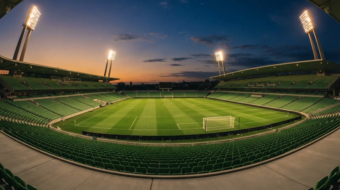 Een leeg voetbalstadion met lichtmasten bij schemering