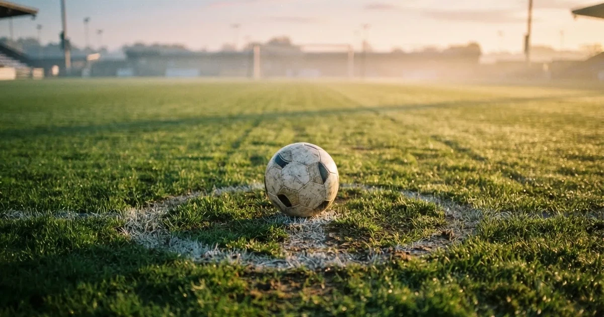 Een voetbal op de middenstip van een grasveld in het ochtendlicht