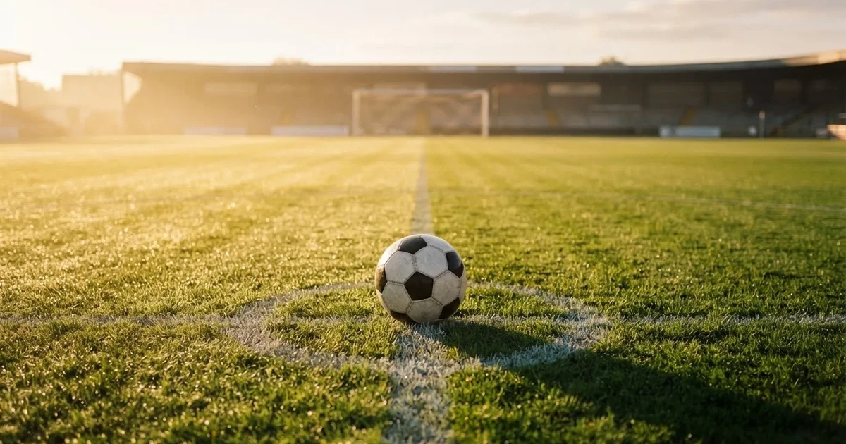 Een voetbal op de middenstip van een grasveld in het ochtendlicht