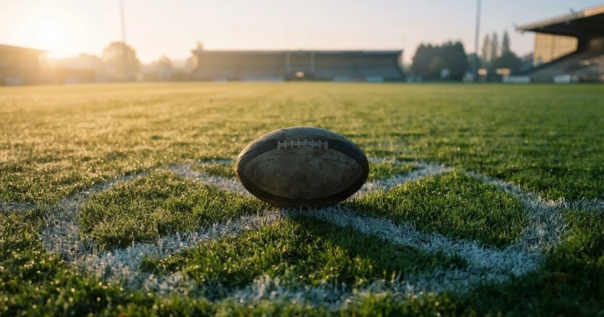 Een voetbal op de middenstip van een grasveld in het ochtendlicht