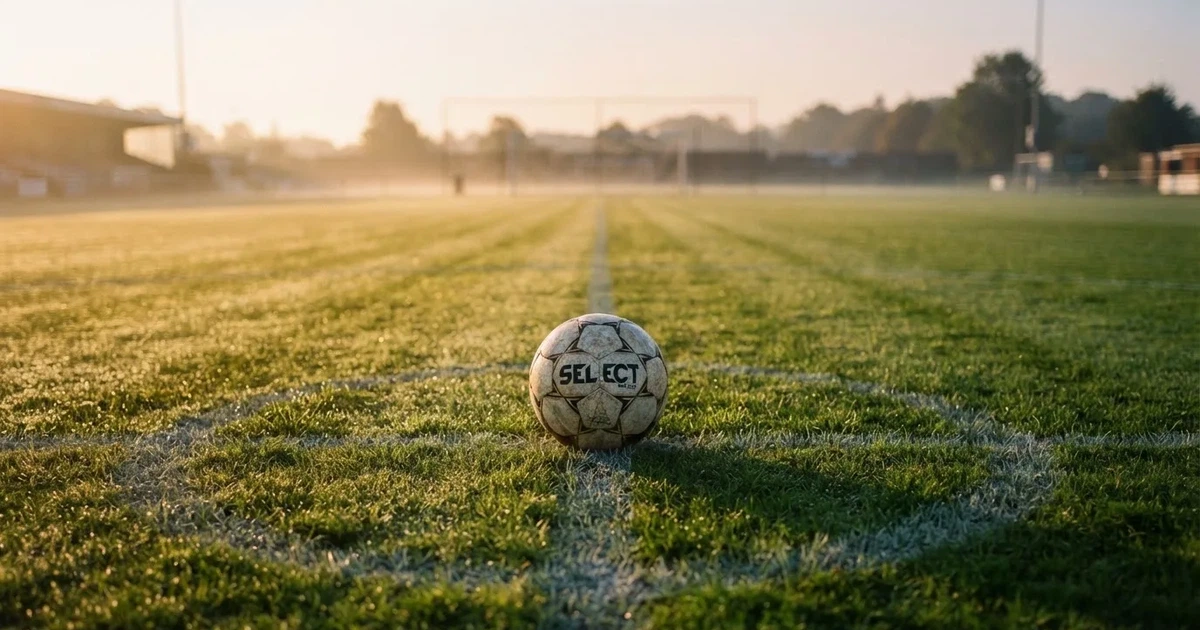 Een voetbal op de middenstip van een grasveld in het ochtendlicht