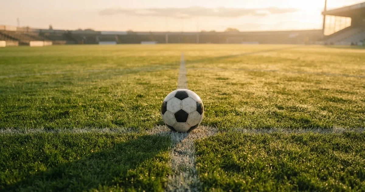 Een voetbal op de middenstip van een grasveld in het ochtendlicht